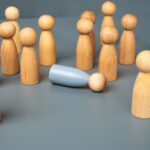 Holzmännchen auf einem grauen Tisch symbolisch für Mediation, wobei ein Männchen umgefallen ist